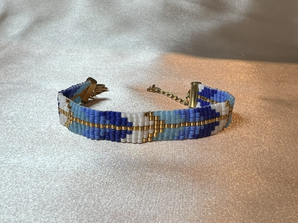 Bunte Perlenarmband mit blauen und goldenen Mustern auf hellem Hintergrund.